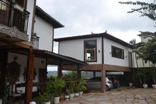 A charming white house with wooden accents and lush greenery exudes a cozy, rustic vibe, perfect for a tranquil getaway in a serene countryside setting.