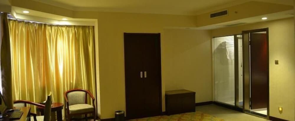 A warmly lit hotel room features golden curtains, wooden furniture, and a glass door leading to another area, creating a cozy atmosphere ideal for travelers seeking comfort and relaxation.