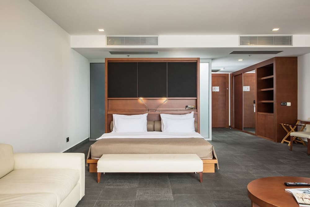 A modern hotel room features a cozy bed with a wooden headboard, sleek furniture, and a minimalist design, ideal for travelers seeking comfort and style in their accommodations.