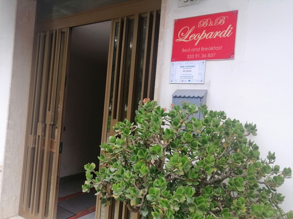 A welcoming entrance to B&B Leopardi, featuring a lush green bush and a red sign, sets an inviting tone for travelers seeking cozy accommodations.