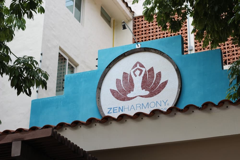 A serene yoga studio entrance features a blue wall with a "Zen Harmony" sign adorned by a lotus flower logo, surrounded by lush greenery, ideal for travelers seeking relaxation and wellness retreats.