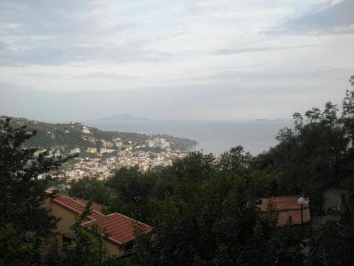 A serene coastal town nestled among lush greenery overlooks the calm sea under a soft sky, ideal for travelers seeking a peaceful retreat with scenic views.