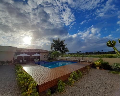 A serene villa retreat features a wooden deck leading to a tranquil pool under a dramatic sky, surrounded by lush greenery and palm trees, ideal for a relaxing vacation getaway.