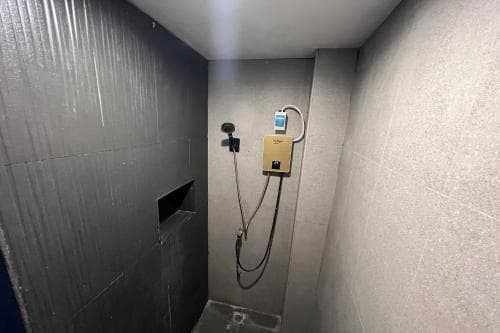 A modern, minimalist shower room with sleek black and white tiled walls, featuring a mounted showerhead and digital controls, exudes a clean and functional vibe ideal for travelers seeking efficient accommodations.