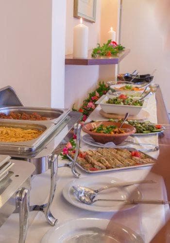 A cozy indoor buffet setup featuring an array of dishes like pasta and salads, adorned with floral decorations and candles, creates a warm and inviting dining atmosphere ideal for travelers seeking a comfortable meal experience.
