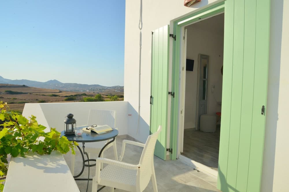 A serene balcony with white furniture and a green door overlooks a tranquil landscape, ideal for a peaceful retreat or vacation rental listing.