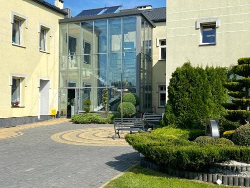 A serene courtyard with a modern glass structure surrounded by lush greenery and benches offers a tranquil urban retreat ideal for business travelers seeking relaxation.