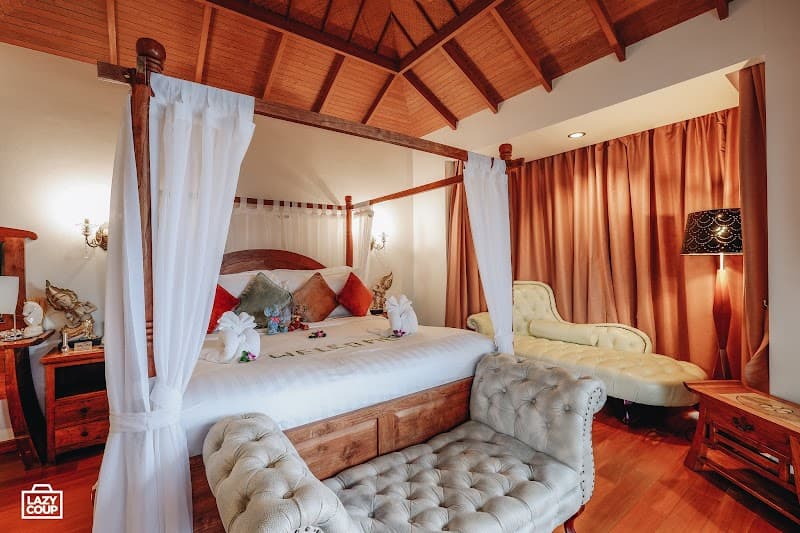 A cozy, luxurious bedroom with a four-poster bed adorned with white curtains, plush seating, and warm lighting creates an inviting atmosphere at Tango Luxe on the beach in Ko Samui, perfect for a romantic getaway.