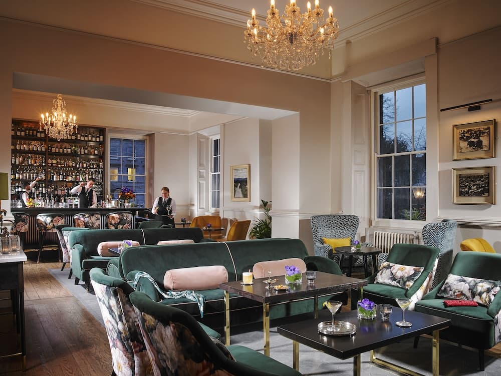 An elegant lounge with plush green sofas, ornate chandeliers, and a well-stocked bar exudes sophistication, perfect for travelers seeking a luxurious relaxation spot during their journey.