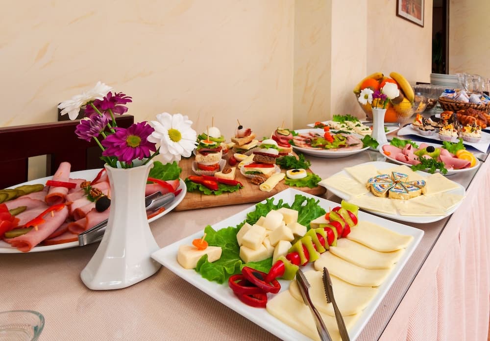 A vibrant buffet table adorned with colorful flowers, assorted cheeses, meats, and appetizers creates an inviting atmosphere perfect for a catered event or banquet setting.
