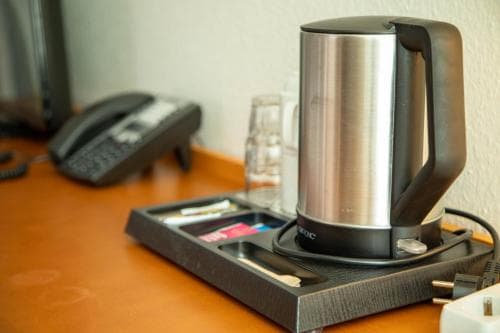 A sleek electric kettle sits on a hotel room desk tray alongside a telephone and water glasses, creating a cozy and functional atmosphere ideal for travelers seeking convenience during their stay.