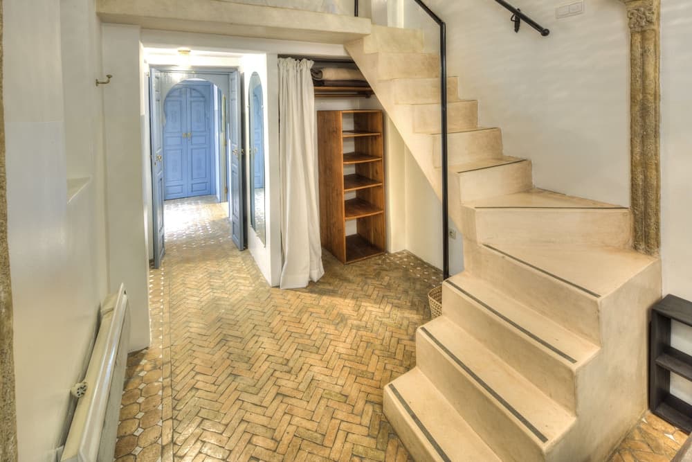A cozy interior hallway with herringbone tile flooring, a staircase leading to an upper level, and a blue door inviting natural light, ideal for travelers seeking charming and historic accommodations.