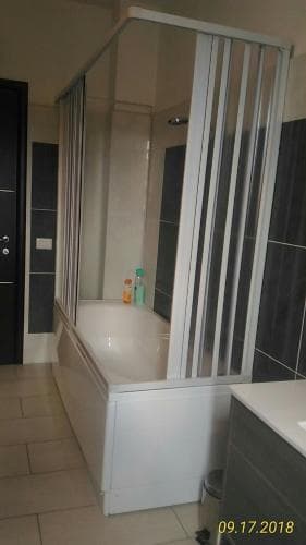 A modern bathroom features a sleek bathtub with a glass shower enclosure, tiled walls, and a minimalist design, ideal for travelers seeking clean and functional accommodations.