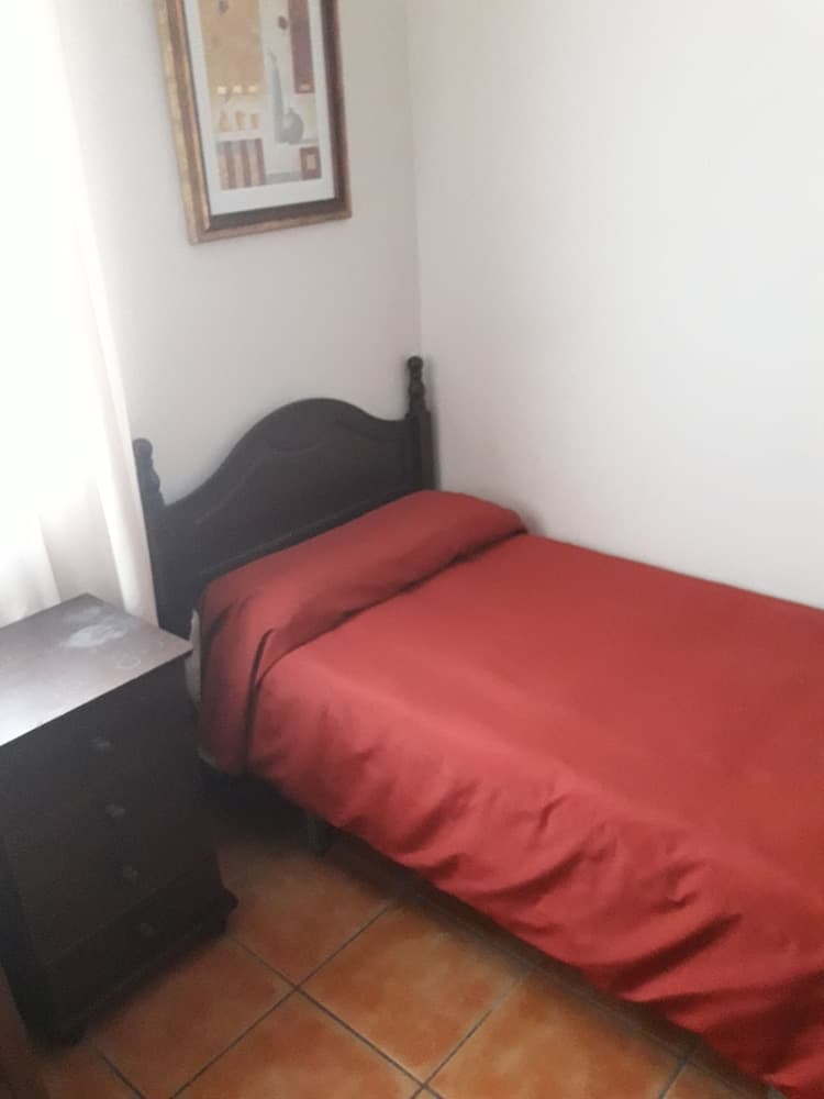 A cozy single bedroom with a red bedspread, wooden furniture, and tiled flooring offers a simple and inviting space for travelers seeking budget-friendly accommodation.
