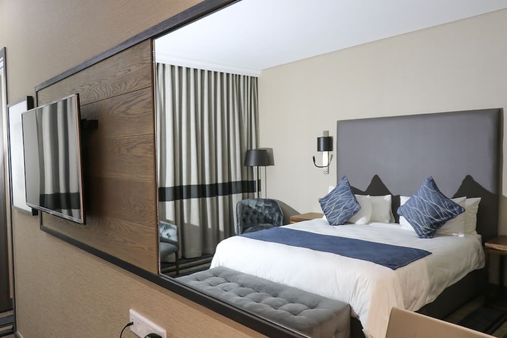A cozy hotel room features a neatly made bed with blue accents, modern furnishings, and a mounted TV, ideal for travelers seeking comfort and style during their stay.