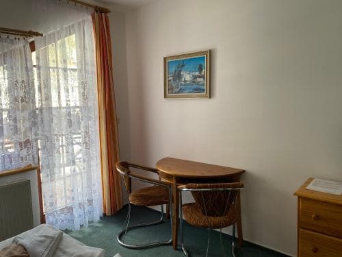 A cozy hotel room features a small wooden table and chairs by a window with lace curtains, creating a serene atmosphere ideal for travelers seeking a quiet retreat.