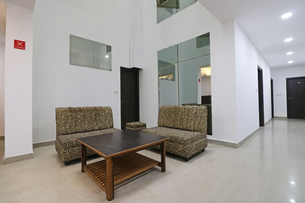 A modern hotel lobby features patterned sofas, a wooden coffee table, and sleek white walls with glass panels, creating a welcoming atmosphere ideal for travelers seeking comfort and style.