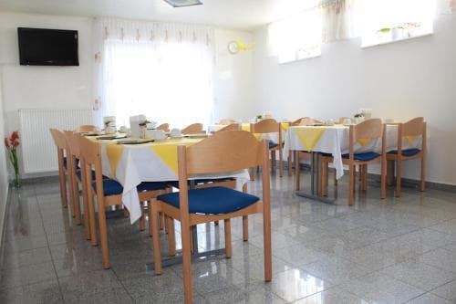A cozy dining room with wooden tables draped in yellow and white tablecloths, blue cushioned chairs, and natural light streaming through curtained windows, ideal for travelers seeking a comfortable breakfast spot.