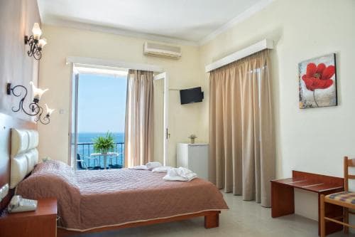 A cozy hotel room with a serene ocean view through a balcony door, featuring warm tones, comfortable furnishings, and vibrant artwork, ideal for travelers seeking relaxation by the sea.