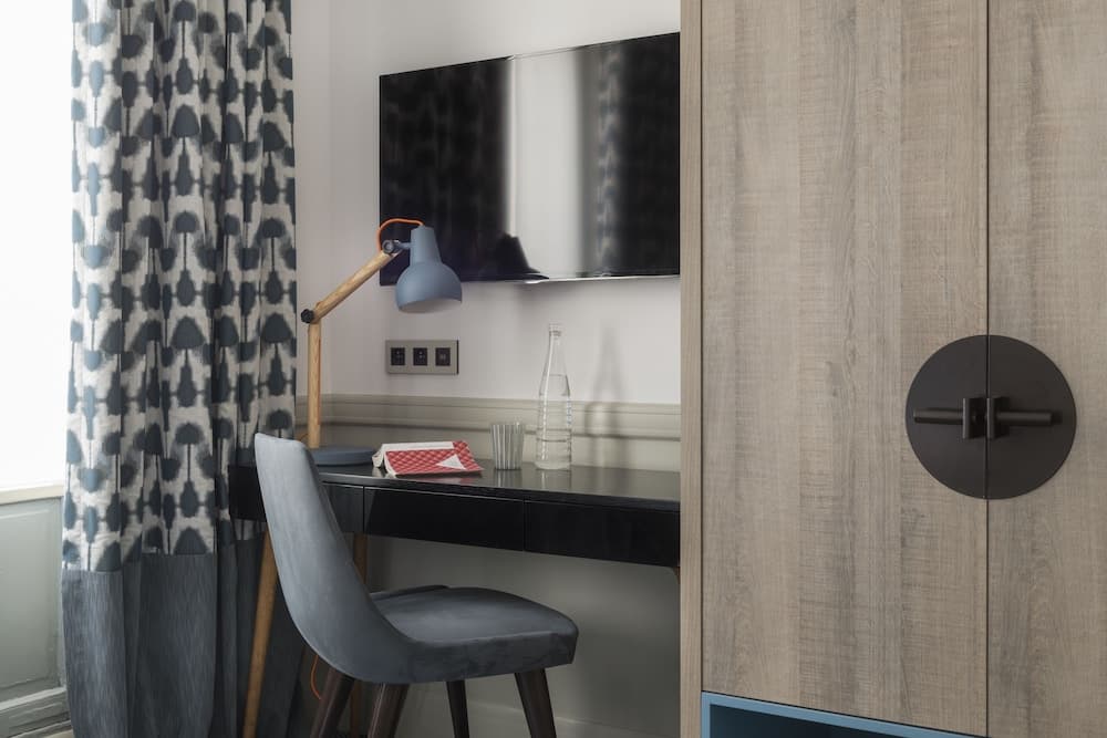 A cozy hotel room workspace features a sleek black desk with a modern lamp, patterned curtains, and a wooden wardrobe, ideal for travelers seeking comfort and functionality.