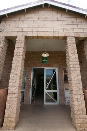 A welcoming entrance to a rustic stone building with sturdy columns and a glass door, ideal for travelers seeking a cozy lodge or community center in a serene setting.