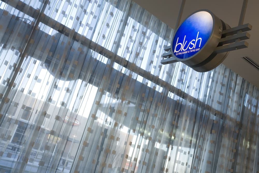 A modern ultralounge and tapas bar named "blush" features a sleek blue sign against a backdrop of patterned sheer curtains, creating an inviting and stylish atmosphere ideal for evening outings or social gatherings.