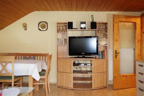 A cozy cabin interior features a wooden entertainment unit with a TV, a dining table set for two, and warm lighting, ideal for a relaxing getaway in a rustic retreat.