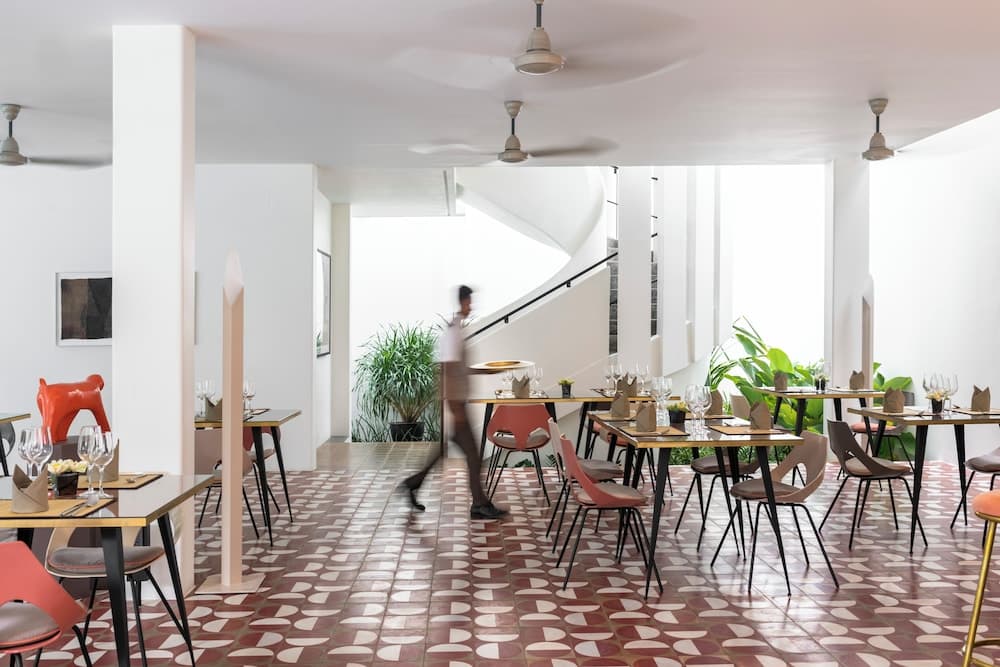 A modern dining area with vibrant tiled floors, sleek furniture, and lush greenery offers a chic ambiance ideal for travelers seeking a stylish restaurant experience.