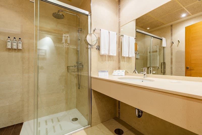 A modern bathroom at Hotel Don Paco in Llanes, Asturias, Spain, features a sleek glass shower, plush towels, and a spacious vanity, creating a serene and inviting atmosphere ideal for travelers seeking comfort and cleanliness.
