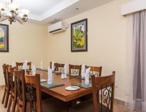 A cozy dining room with wooden tables set for a meal, adorned with colorful artwork and a chandelier, offers an inviting atmosphere for travelers seeking a comfortable space for group gatherings or family dinners.