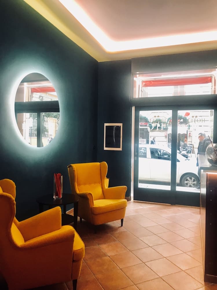 A cozy hotel lobby features vibrant yellow armchairs near a circular window, set against dark walls with warm lighting, creating an inviting atmosphere ideal for travelers seeking relaxation.