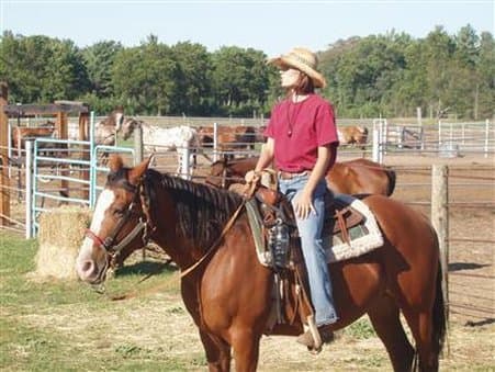 A serene rural ranch scene features a rider on a chestnut horse, surrounded by fenced paddocks, hay bales, and trees, ideal for equestrian enthusiasts seeking a peaceful countryside getaway.