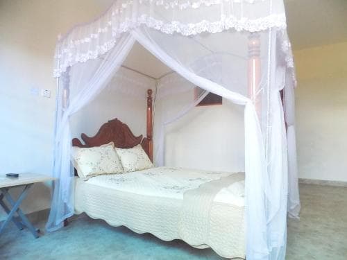 A cozy bedroom with a four-poster bed draped in white mosquito netting creates a serene and inviting atmosphere, perfect for travelers seeking a peaceful retreat.