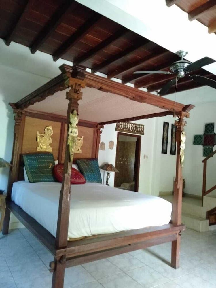A cozy bedroom with a traditional wooden four-poster bed adorned with intricate carvings, set under a vaulted ceiling, exudes a warm and inviting atmosphere ideal for travelers seeking cultural immersion in a rustic retreat.