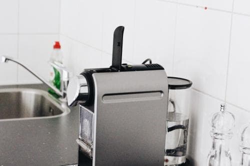 A sleek espresso machine sits on a modern kitchen countertop beside a sink and glass containers, creating a clean and functional atmosphere ideal for coffee enthusiasts exploring culinary travel experiences.