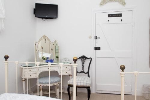 A cozy bedroom corner features a vintage vanity with a mirror, a checkered chair, and a white door, creating a serene and elegant atmosphere ideal for boutique hotel stays.
