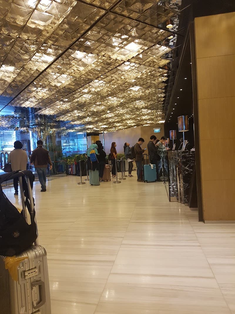 Travelers queue under a shimmering glass ceiling in the modern lobby of The Kowloon Hotel in Tsim Sha Tsui, Hong Kong, creating an elegant and bustling atmosphere ideal for business and leisure stays.
