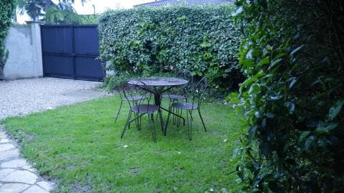 A serene backyard garden features a cozy outdoor seating area with a glass table and chairs surrounded by lush greenery, ideal for a peaceful retreat or a quiet getaway.