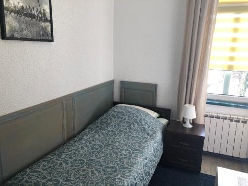 A cozy hotel room features a neatly made bed with patterned bedding, a bedside table with a lamp, and a window with striped curtains, ideal for travelers seeking comfort and simplicity.