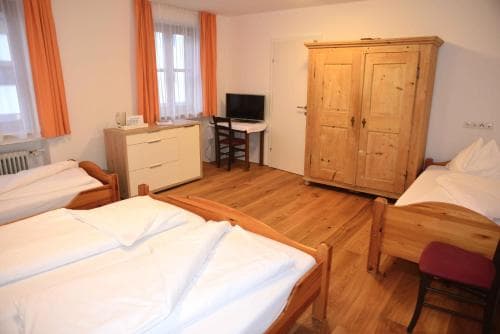 A cozy hostel room with wooden furniture, orange curtains, and neatly arranged beds offers a comfortable and budget-friendly stay for travelers seeking simplicity and warmth.