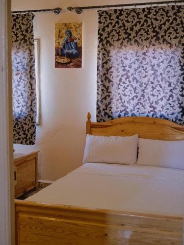 A cozy bedroom with patterned curtains, a wooden bed, and a serene wall art piece offers a tranquil retreat for travelers seeking comfort and relaxation.