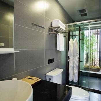 A modern bathroom with sleek gray tiles, a glass-enclosed shower featuring hanging robes, and a serene view of greenery outside, ideal for travelers seeking comfort and relaxation in a hotel setting.