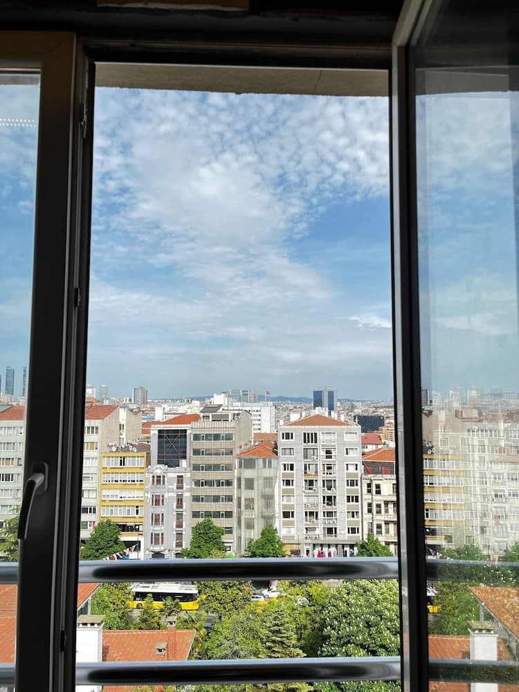 A serene urban view framed by an open window showcases a vibrant cityscape under a partly cloudy sky, ideal for travelers seeking a peaceful yet lively accommodation experience.