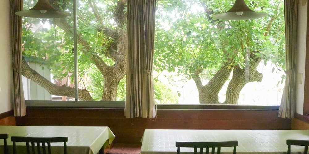 A serene dining area with wooden tables and chairs framed by large windows showcasing lush green trees, ideal for travelers seeking a peaceful retreat in nature.