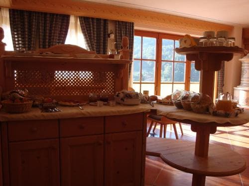 A cozy breakfast nook bathed in sunlight features rustic wooden furniture, fresh bread, and a scenic view through large windows, ideal for travelers seeking a warm and inviting start to their day.