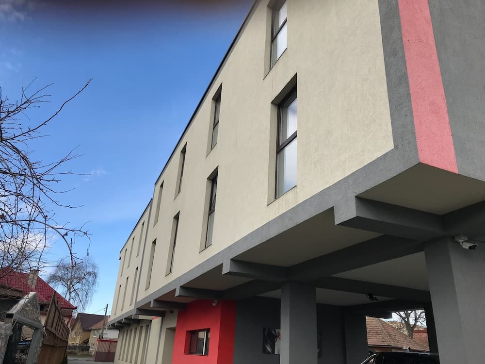 A modern multi-story building with beige walls, red accents, and large windows stands under a clear blue sky, offering an urban residential or commercial space ideal for city living or business ventures.
