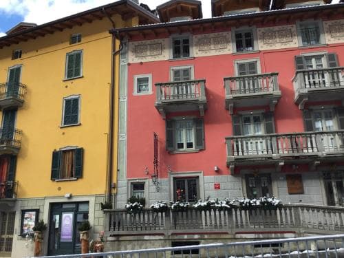 A charming European riverside scene features colorful buildings with balconies adorned with flowers, evoking a cozy and picturesque atmosphere ideal for leisurely strolls and cultural exploration.