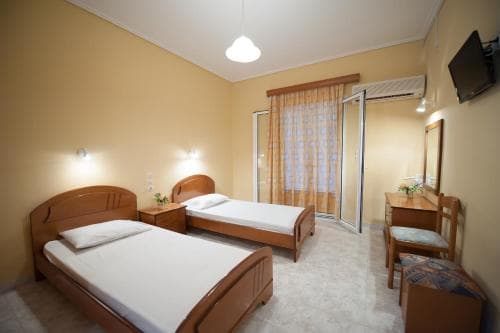 A cozy hotel room with two wooden beds, a desk, and a sliding glass door leading to a balcony, ideal for travelers seeking comfort and simplicity in their accommodation.