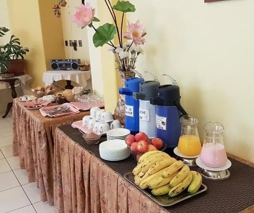 A cozy indoor breakfast buffet setup features fresh fruits, beverages, and pastries on patterned tables, creating a welcoming atmosphere ideal for travelers seeking a comfortable morning meal experience.