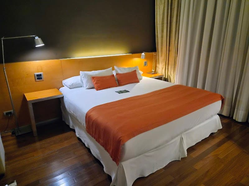 A cozy hotel room in Buenos Aires features a neatly made bed with orange accents, wooden flooring, and soft lighting, ideal for travelers seeking comfort and relaxation.